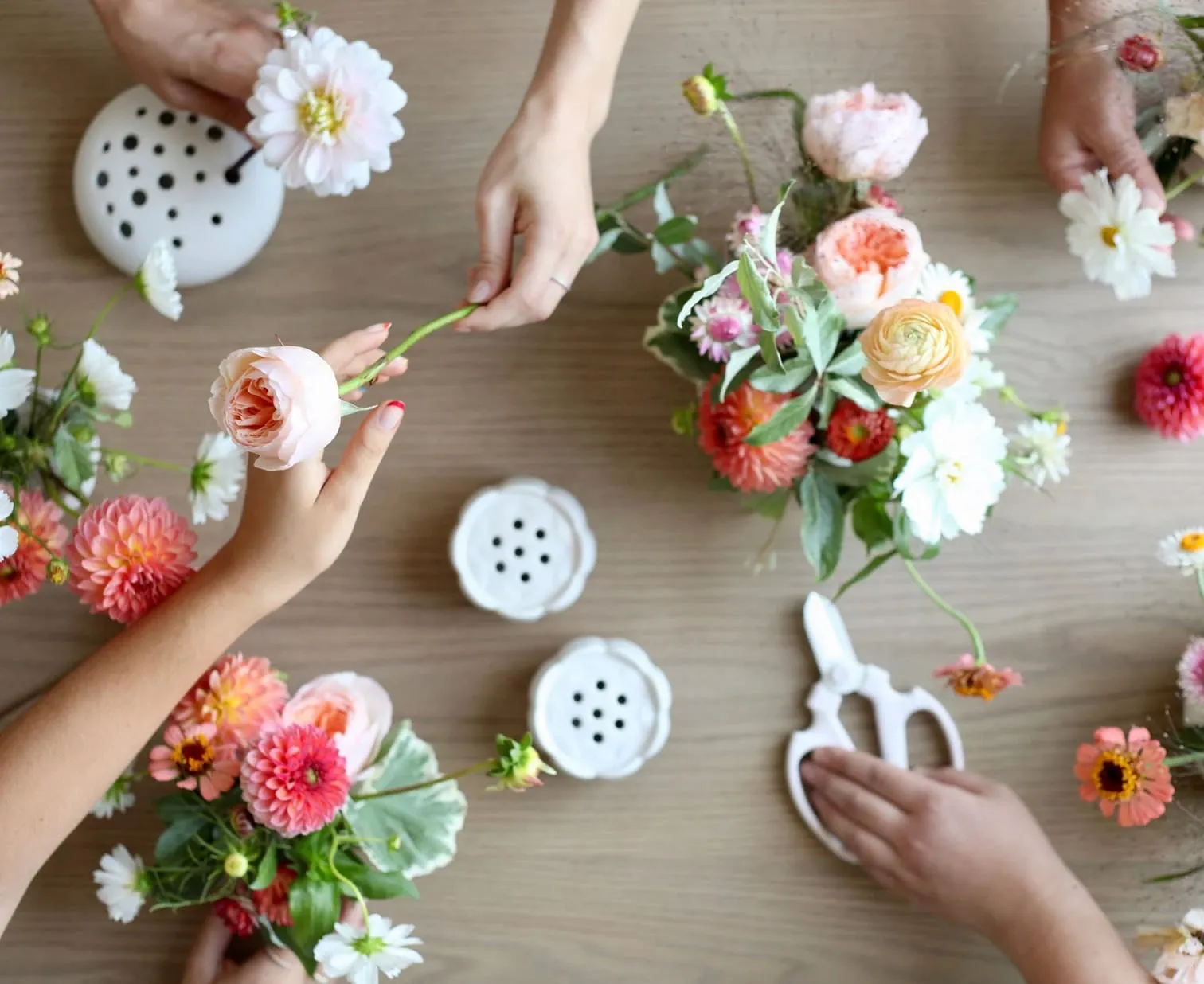 Hands arranging fresh-cut flowers at a Floral Society workshop table